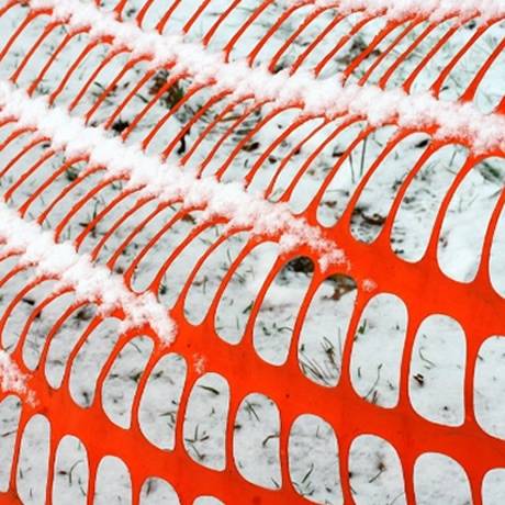 Orange plastic netting with rectangle opening used as snow fence, and white snow on it.