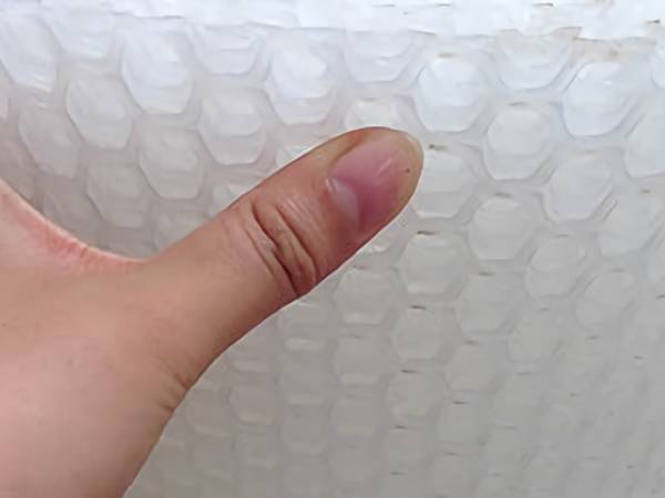 A roll of transparent hexagonal plastic flat netting and a hand on it