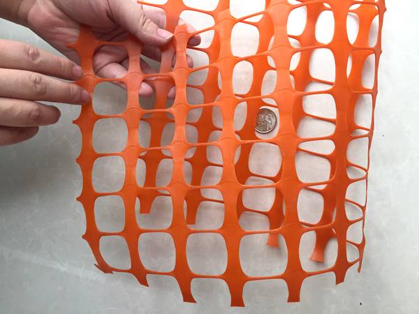 A hand is holding a piece of folded orange plastic mesh barrier.