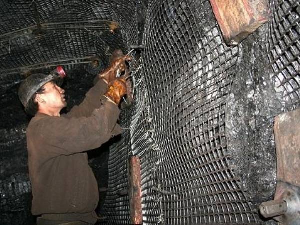 A worker is fixing plastic support net in underground coal mine.