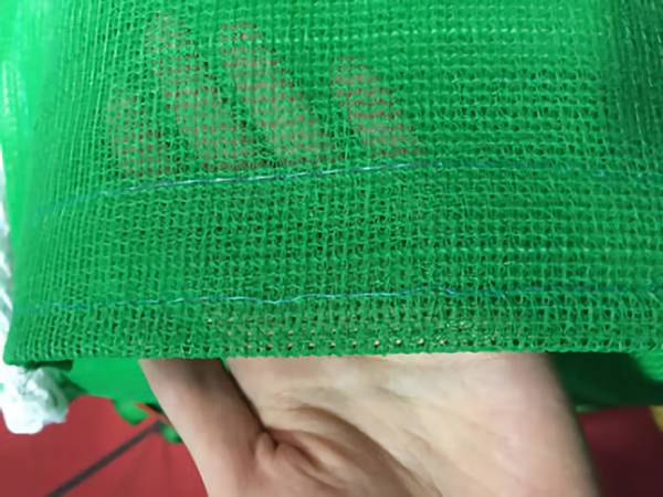 A piece of green knitted sun shade netting with reinforced edge on a hand.